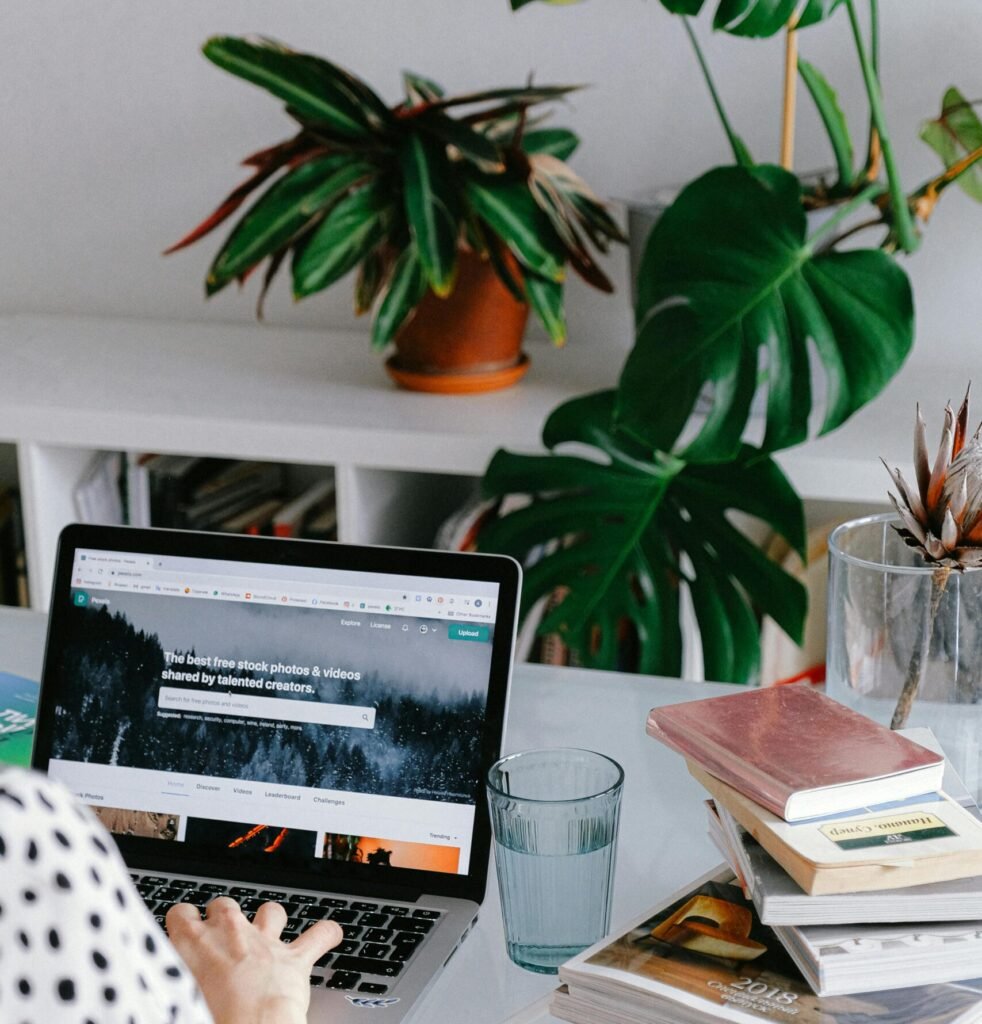 A woman working from home on her laptop surrounded by plants and books for a cozy office feel.